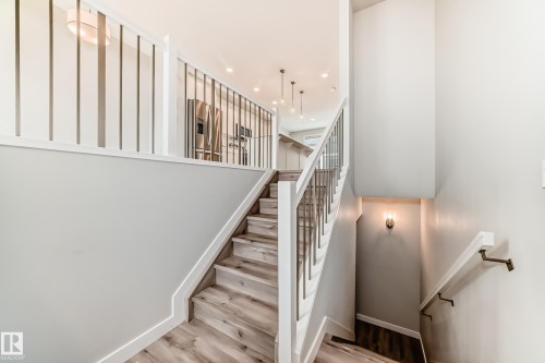Staircase featuring wood-finish treads, white risers, and a contemporary railing with white newel posts and metal balusters - 26 1729 Keene Crescent, Edmonton, AB 