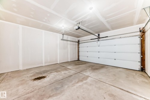 Spacious garage featuring a concrete floor, white panel garage door, and ceiling-mounted lighting - 26 1729 Keene Crescent, Edmonton, AB 