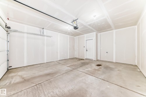 Spacious two-car garage featuring a concrete floor, an overhead garage door, built-in lighting, and an interior access door - 26 1729 Keene Crescent, Edmonton, AB 