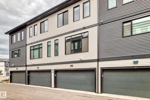 Modern multi-level exterior featuring horizontal siding in contrasting light and dark tones, black window frames, dark garage doors, and exterior lighting fixtures - 26 1729 Keene Crescent, Edmonton, AB 