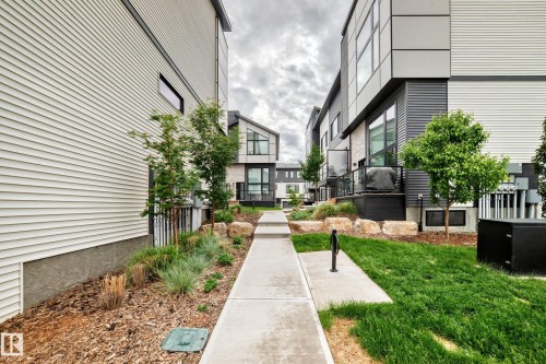 Modern townhome exterior showcasing a concrete pathway, grass lawn, and landscaped garden beds - 26 1729 Keene Crescent, Edmonton, AB 