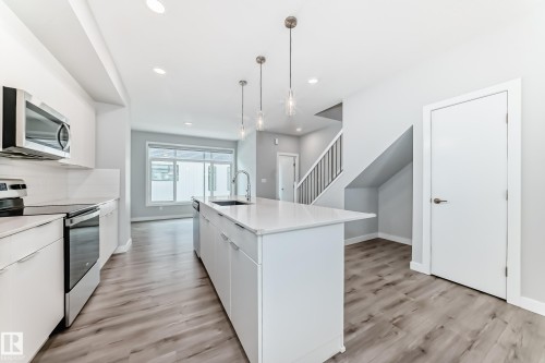 Open concept kitchen featuring an island with a built-in sink and pendant lighting, stainless steel appliances, wood-finish flooring, and recessed ceiling lights - 26 1729 Keene Crescent, Edmonton, AB 
