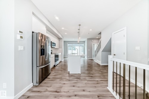 Open-concept living space featuring wood-finish flooring, white walls, and a contemporary kitchen with stainless steel appliances - 26 1729 Keene Crescent, Edmonton, AB 