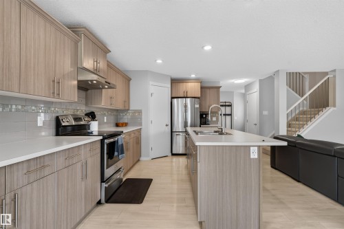 Kitchen featuring wood-finish cabinetry, stainless steel appliances, a center island with a sink, and light wood-finish flooring - 4612 Westcliff Point(E), Edmonton, AB 
