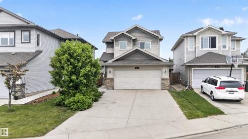 Front exterior featuring light gray siding, stone accents, a two-car garage, concrete driveway, and mature landscaping - 4612 Westcliff Point(E), Edmonton, AB 
