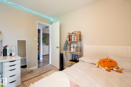 Neutral-toned bedroom featuring wall-to-wall carpeting and a spacious doorway opening to a utility area with shelving and a washer - 8 2703 79 Street, Edmonton, AB 