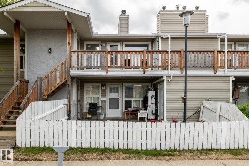 Multi-level residential exterior featuring horizontal siding, a private balcony with wood railing, and a ground-level patio enclosed by a white picket fence - 8 2703 79 Street, Edmonton, AB 