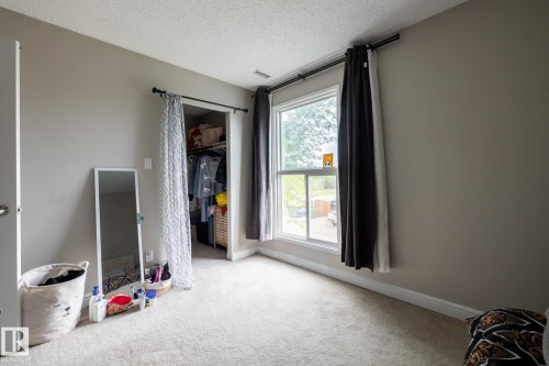 Carpeted interior room featuring a window with a black curtain rod, light gray wall paint, white baseboards, and a visible closet opening - 8 2703 79 Street, Edmonton, AB 