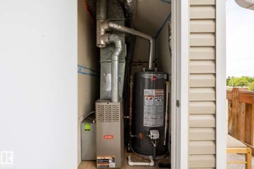 Dedicated utility closet featuring a water heater and furnace with exposed ductwork, housed within a compact space with beige siding visible on the exterior wall - 8 2703 79 Street, Edmonton, AB 