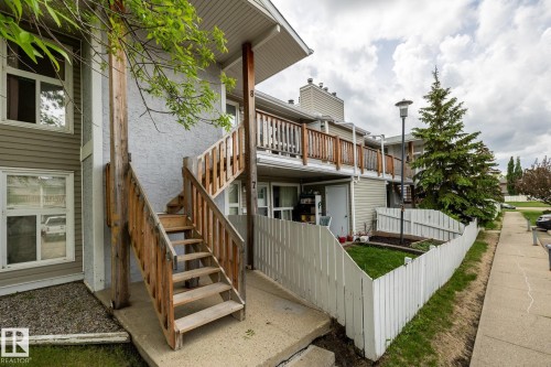 Multi-level townhome exterior featuring wood-tone railings and stairs, a white picket fence, and mature landscaping - 8 2703 79 Street, Edmonton, AB 