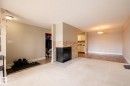 Living area featuring a floor-to-ceiling stone-faced fireplace with a hearth, light-toned carpeting, and wood-finish flooring - 8 2703 79 Street, Edmonton, AB 