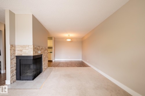 Living area featuring a corner fireplace with a stone-tile surround and a light-colored hearth - 8 2703 79 Street, Edmonton, AB 