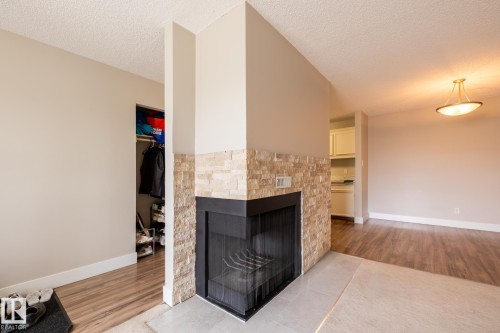 Corner fireplace featuring a stacked stone surround and black hearth, wood-finish flooring, and a semi-flush ceiling fixture - 8 2703 79 Street, Edmonton, AB 