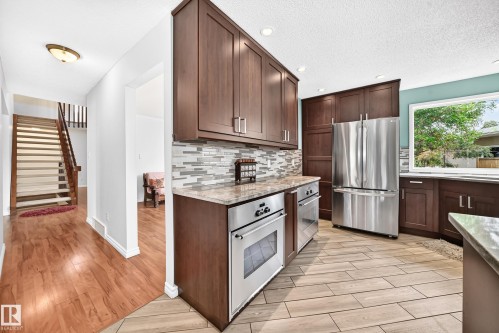 Modern kitchen featuring rich wood-finish cabinetry, stainless steel appliances, and light-toned countertops - 8224 186 Street Nw, Edmonton, AB 