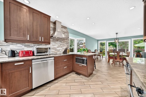 Modern kitchen featuring wood-finish cabinetry, light-toned granite countertops, a stainless steel dishwasher, and a built-in microwave - 8224 186 Street Nw, Edmonton, AB 