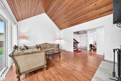 Spacious living area featuring a vaulted wood-finish ceiling, wood-finish flooring, white walls, and a fireplace with a light-toned hearth - 8224 186 Street Nw, Edmonton, AB 