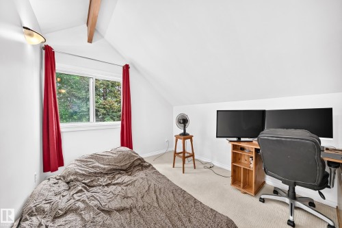 Sloped ceiling room featuring a double-pane window, wall-mounted light fixture, visible ceiling beam, and neutral-toned carpeting - 8224 186 Street Nw, Edmonton, AB 