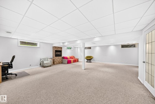 Spacious lower level featuring textured carpeting, a stone-accented fireplace, recessed lighting, and multiple windows - 8224 186 Street Nw, Edmonton, AB 