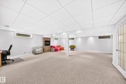 Spacious lower level featuring textured carpeting, a stone-accented fireplace, recessed lighting, and multiple windows - 