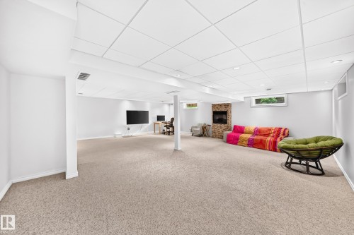 Spacious finished room with light-colored carpeting, recessed lighting, and a stone-faced fireplace - 8224 186 Street Nw, Edmonton, AB 