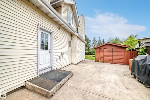 Expansive concrete patio with a detached wooden storage shed, featuring neutral vinyl siding on the property exterior and a white exterior door - 8224 186 Street Nw, Edmonton, AB 