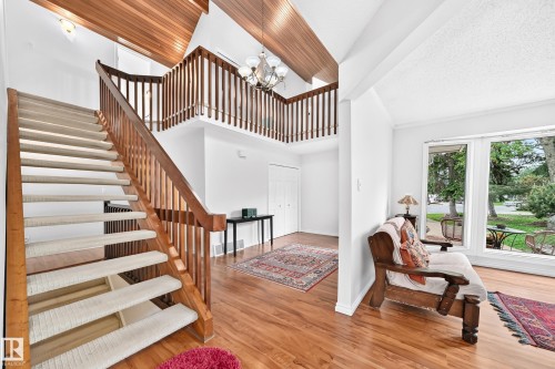 Two-story entryway featuring a wood staircase with carpeted treads, wood-finish flooring, a vaulted wood-paneled ceiling, and a second-story overlook with wood railings - 8224 186 Street Nw, Edmonton, AB 