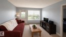 Open living area featuring a large window with horizontal blinds, a glass-paneled exterior door, and light-toned carpeting - 202 13635 34 Street, Edmonton, AB 