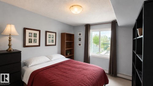Bedroom featuring a window with exterior visibility, light gray wall paint, and ceiling-mounted lighting - 202 13635 34 Street, Edmonton, AB 