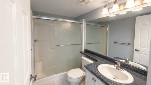 Bathroom featuring a vanity with an oval sink, a blue speckled countertop, and a large mirror with a four-light fixture - 202 13635 34 Street, Edmonton, AB 