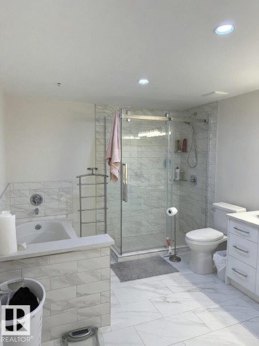 Bathroom featuring a glass-enclosed shower, a built-in soaking tub, a vanity with under-counter storage, recessed lighting, and large format floor tiling - 305 11111 82 Avenue, Edmonton, AB 