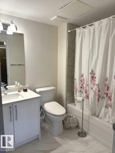 Bathroom featuring a white vanity with an integrated sink, a large wall-mounted mirror, and a white toilet - 305 11111 82 Avenue, Edmonton, AB 