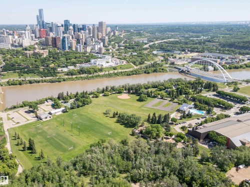 Aerial perspective showcasing the city skyline, a river, a prominent bridge, expansive green spaces, and a recreational facility with an outdoor pool - 305 11111 82 Avenue, Edmonton, AB 