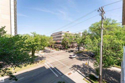 Urban streetscape featuring a multi-lane intersection with pedestrian crosswalks, surrounding mature trees, and commercial buildings - 305 11111 82 Avenue, Edmonton, AB 