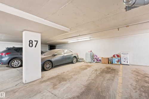 Dedicated parking space within a subterranean garage, featuring concrete flooring and overhead fluorescent lighting - 305 11111 82 Avenue, Edmonton, AB 