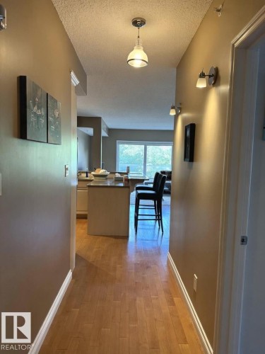 Hallway featuring wood-finish flooring, warm-toned wall paint, and white trim - 305 11111 82 Avenue, Edmonton, AB 