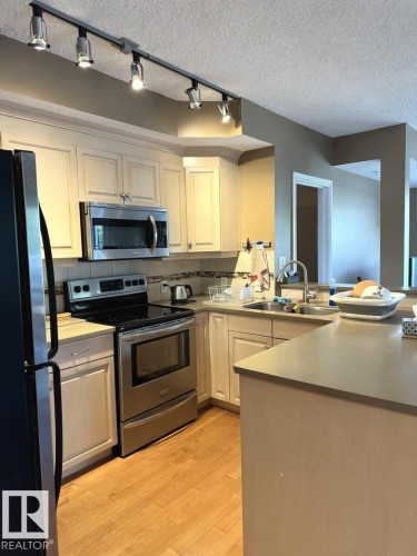 Kitchen featuring wood-finish flooring, stainless steel appliances, light-toned cabinetry, track lighting, and a neutral countertop - 305 11111 82 Avenue, Edmonton, AB 