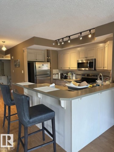 Kitchen featuring light-toned cabinetry, stainless steel appliances, a multi-level breakfast bar with a neutral countertop, and wood-finish flooring - 305 11111 82 Avenue, Edmonton, AB 