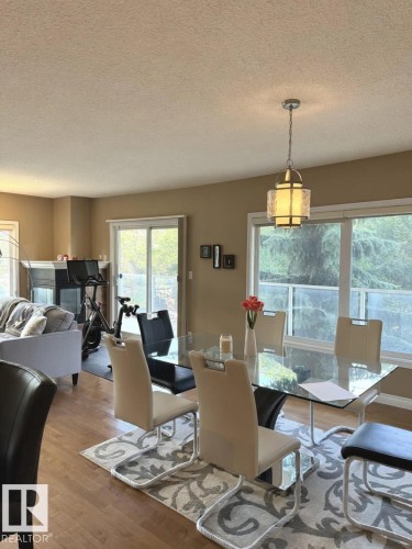 Open-concept living area featuring wood-finish flooring, a modern chandelier, and large windows with sliding glass door access - 305 11111 82 Avenue, Edmonton, AB 
