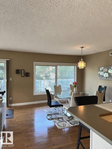 Open-concept living area with wood-finish flooring, a large picture window, and a sliding glass door - 305 11111 82 Avenue, Edmonton, AB 