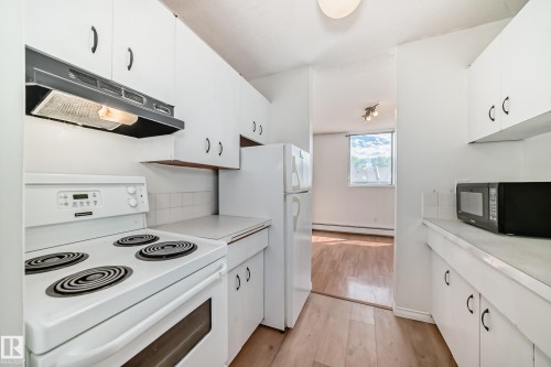 Kitchen featuring white cabinetry, white electric range, white refrigerator, and wood-finish flooring - 401 11007 83 Avenue, Edmonton, AB 