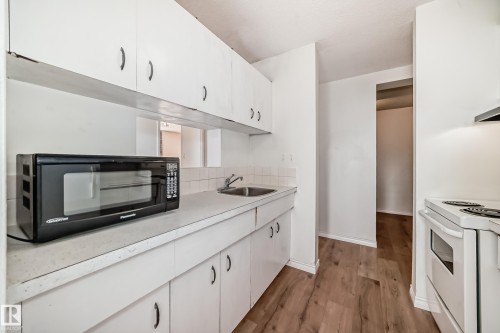 Kitchen featuring white cabinetry, white countertops, a stainless steel sink, tile backsplash, and wood-finish flooring - 401 11007 83 Avenue, Edmonton, AB 