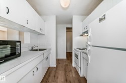 Galley kitchen featuring white cabinetry, white appliances including a refrigerator and electric range, laminate countertops, a stainless steel sink, and wood-finish flooring - 