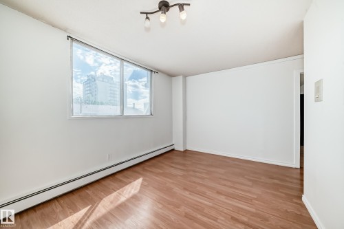 Open room featuring wood-finish flooring, white walls, and a large window with a building backdrop - 401 11007 83 Avenue, Edmonton, AB 