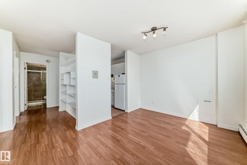 Open-concept living space featuring wood-finish flooring, built-in shelving, track lighting, and white walls - 401 11007 83 Avenue, Edmonton, AB 