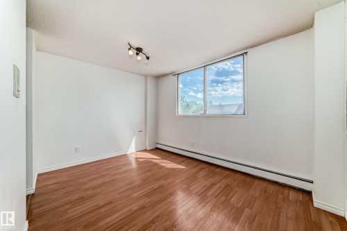 Spacious room featuring wood-finish flooring, a large window, and track lighting - 401 11007 83 Avenue, Edmonton, AB 