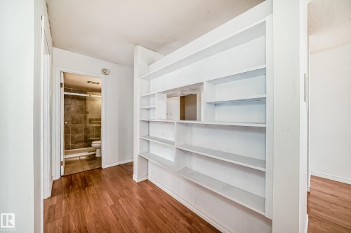 Built-in shelving unit with multiple compartments, wood-finish flooring, and a full bathroom featuring tiled walls and a glass-enclosed shower - 401 11007 83 Avenue, Edmonton, AB 