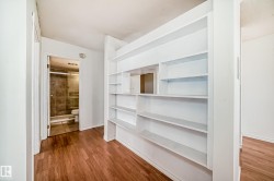 Built-in shelving unit with multiple compartments, wood-finish flooring, and a full bathroom featuring tiled walls and a glass-enclosed shower - 