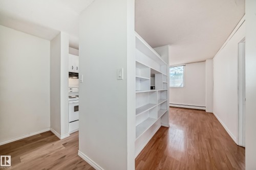 Built-in shelving unit with multiple compartments, wood-finish flooring, white baseboards, and a window providing natural illumination - 401 11007 83 Avenue, Edmonton, AB 