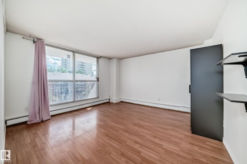 Spacious room featuring wood-finish flooring, a large sliding glass door, and white painted walls - 401 11007 83 Avenue, Edmonton, AB 