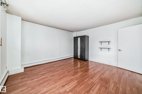 Spacious room featuring wood-finish flooring, white walls, and a textured white ceiling - 401 11007 83 Avenue, Edmonton, AB 